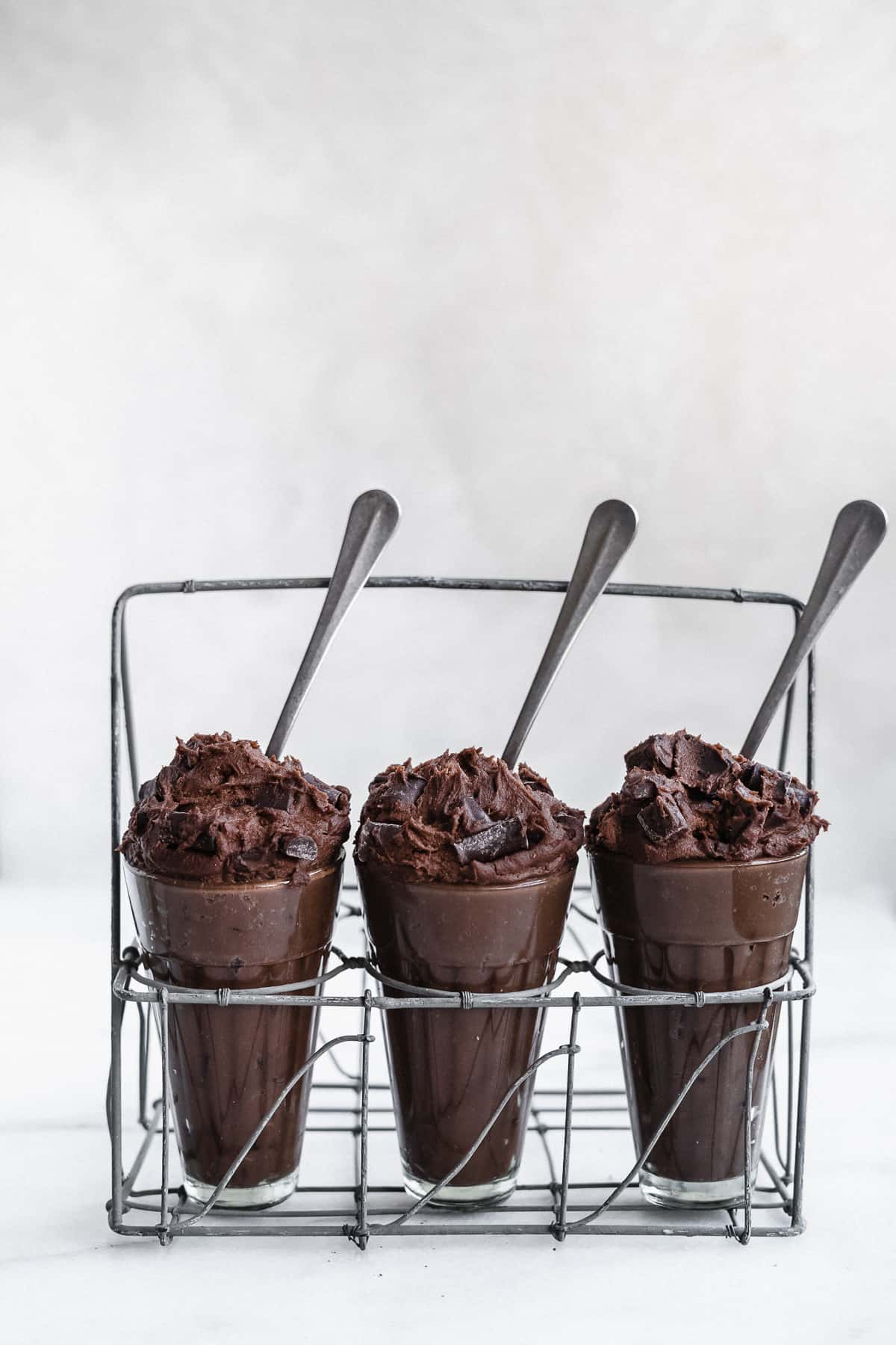 Three glasses with edible brownie batter in a drink caddy with spoons sticking out of the side.