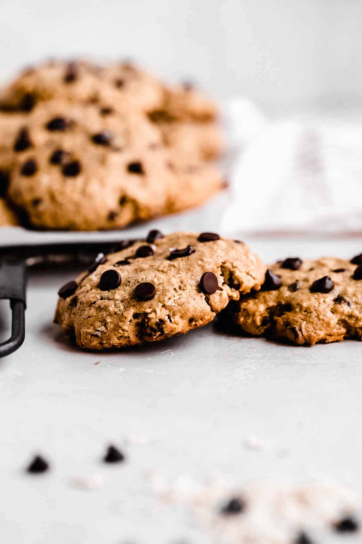 Side view image of two Oatmeal Chocolate Chip Cookies on a marble slab. Additional cookies are on a cooling rack on the background.