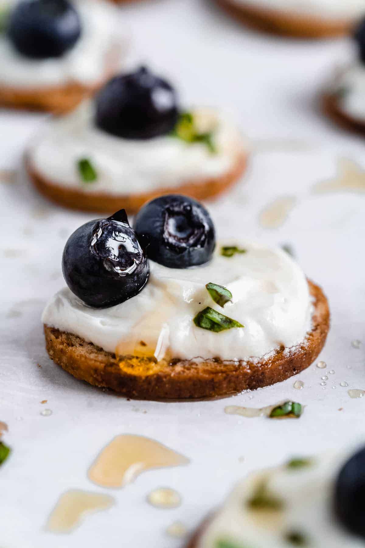 Closeup image of Honey Whipped Goat Cheese spread on an Angelic Bakehouse crisp.  Two blueberries are o top!  