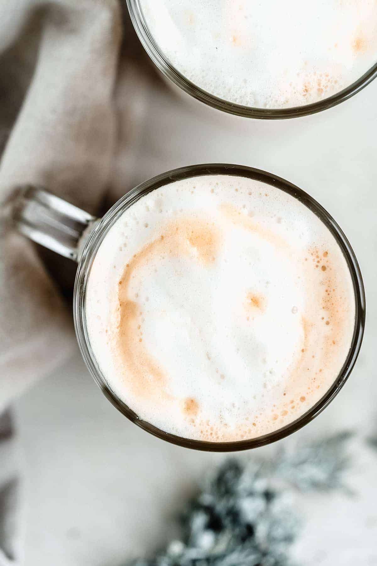 Overhead image of a clear mug filled with Maple Sea Salt Almond Milk Latte to highlight the foam on top.  