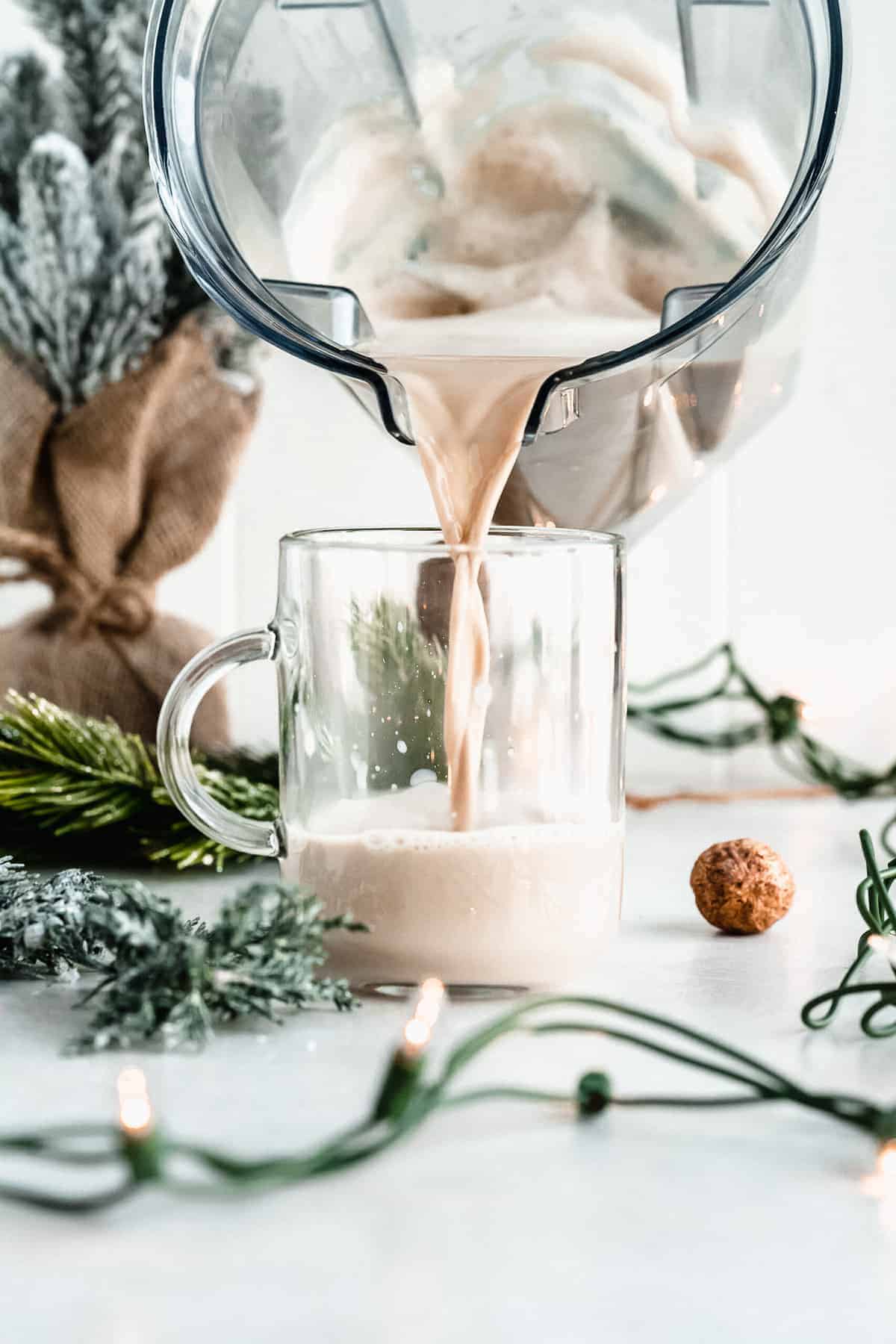 Side view photo of a clear mug sitting on a marble slab.  A food processor pitcher is above pouring the Maple Sea Salt Almond Milk Latte into the mug.  