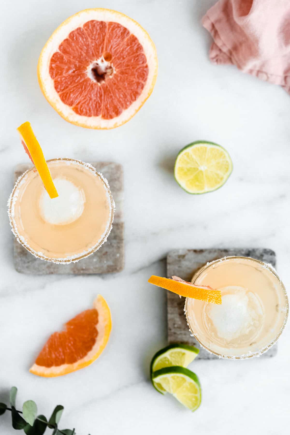 Overhead photo of two Skinny Smoky Grapefruit Margaritas served in crystal glasses sitting on marble coasters.  The glasses have salted rims and are garnished with a slice of grapefruit.  