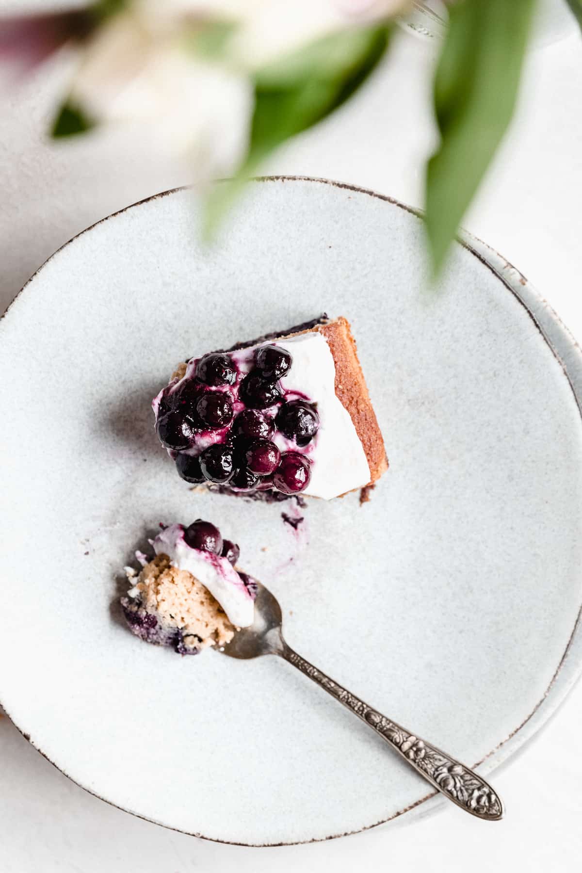 Overhead photo of a single serving of Blueberry Vanilla Sheet Cake on a gray plate with a silver fork laying nearby with a bite of cake on the fork.  