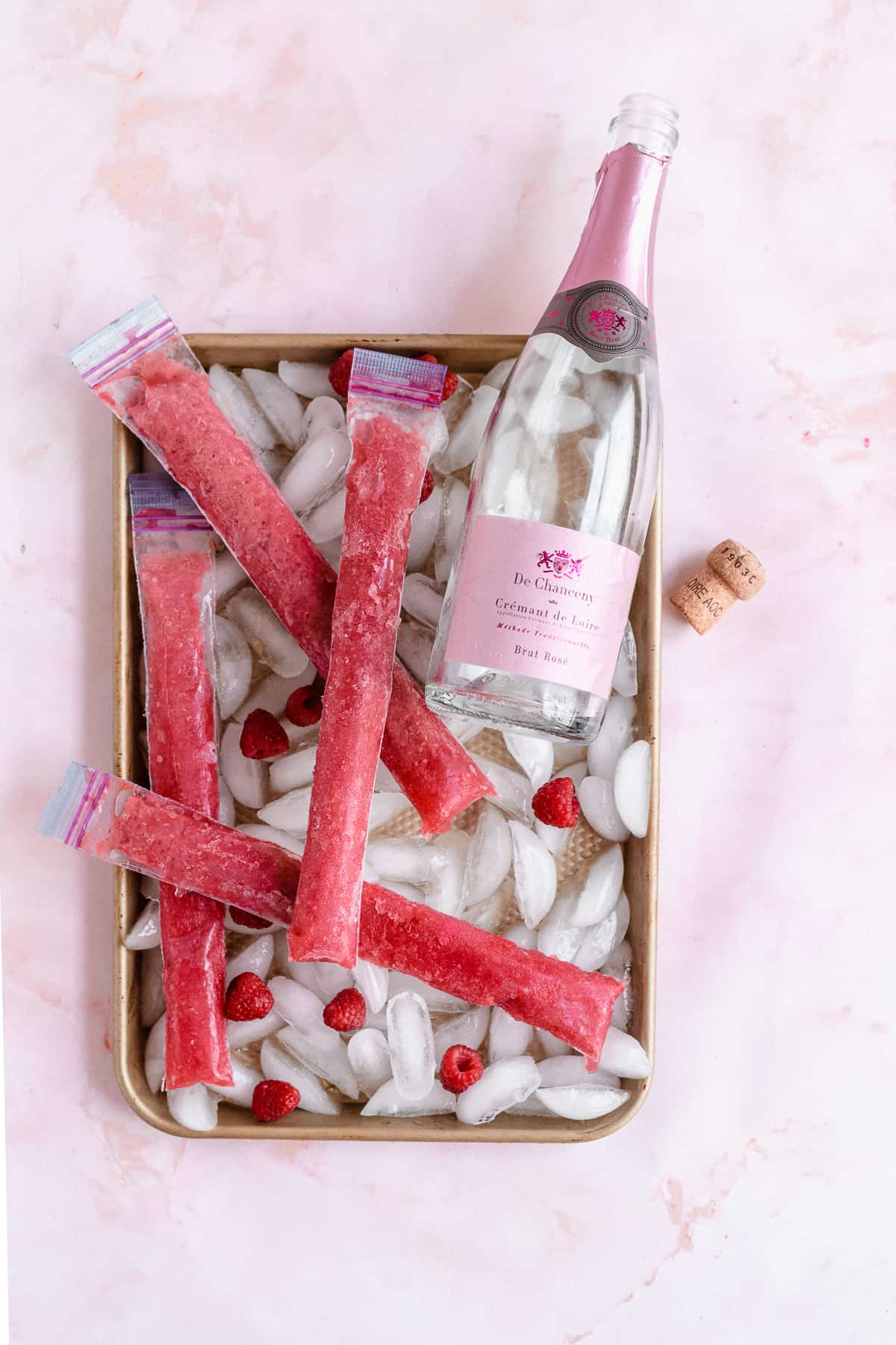 Frozen pink ice pops over ice with bottle of rose'.