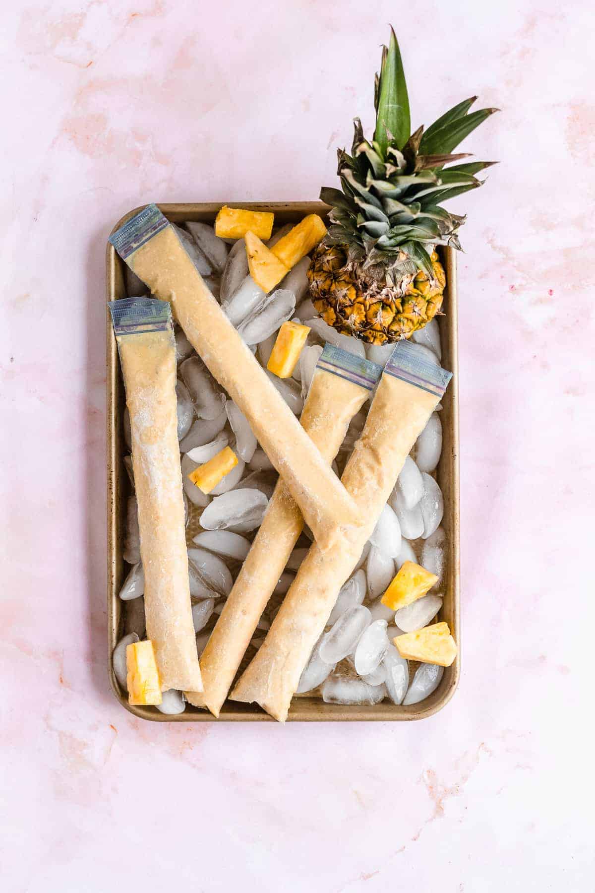 Frozen pineapple ice pops on a sheet with ice.