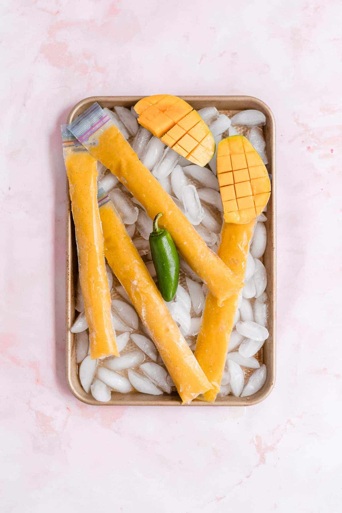 Frozen orange ice pops on a sheet with ice.