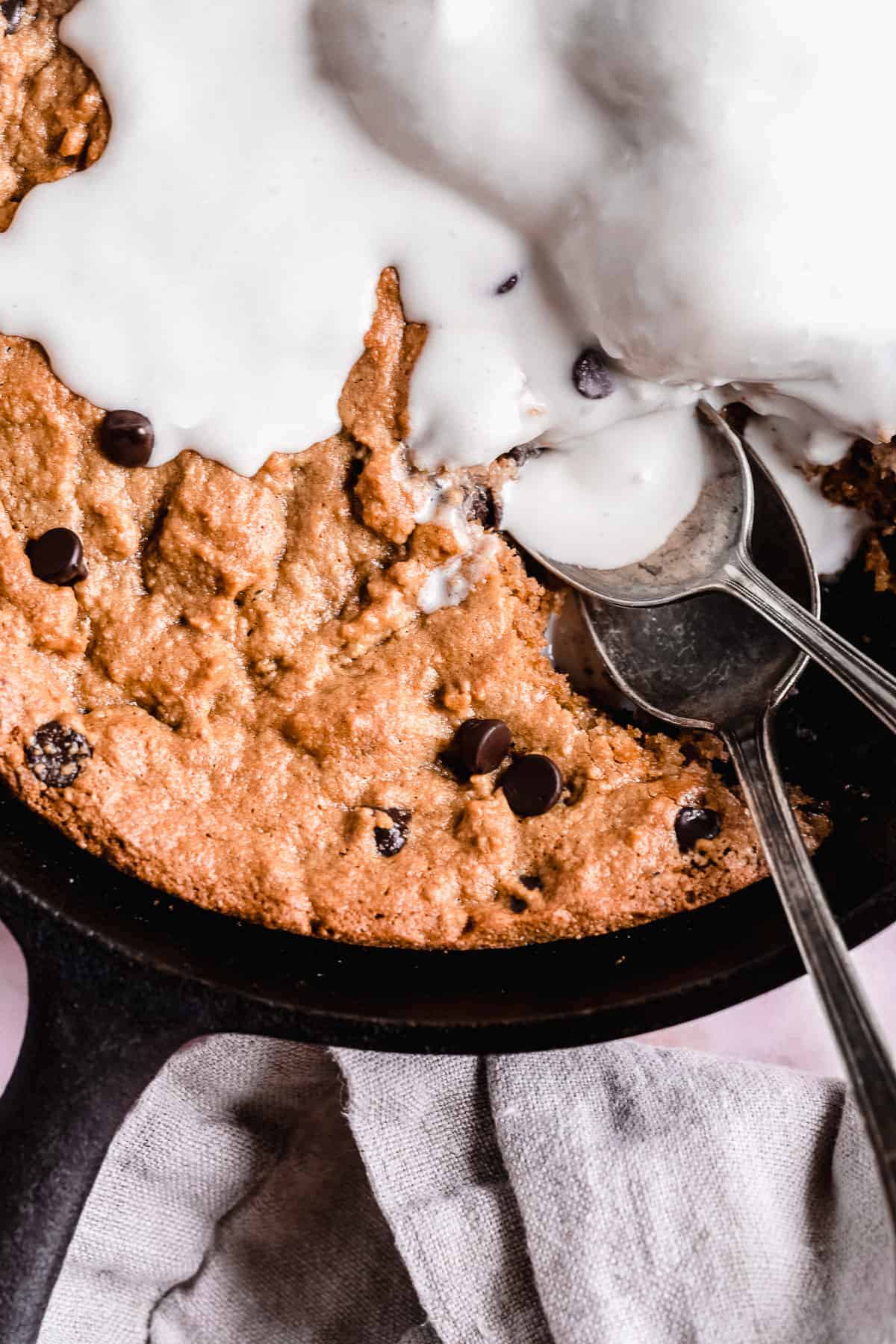 Close up image of Paleo Chocolate Chip Cookie Skillet served a la mode with vanilla ice cream melting on top.  Two spoons are laying nearby.  