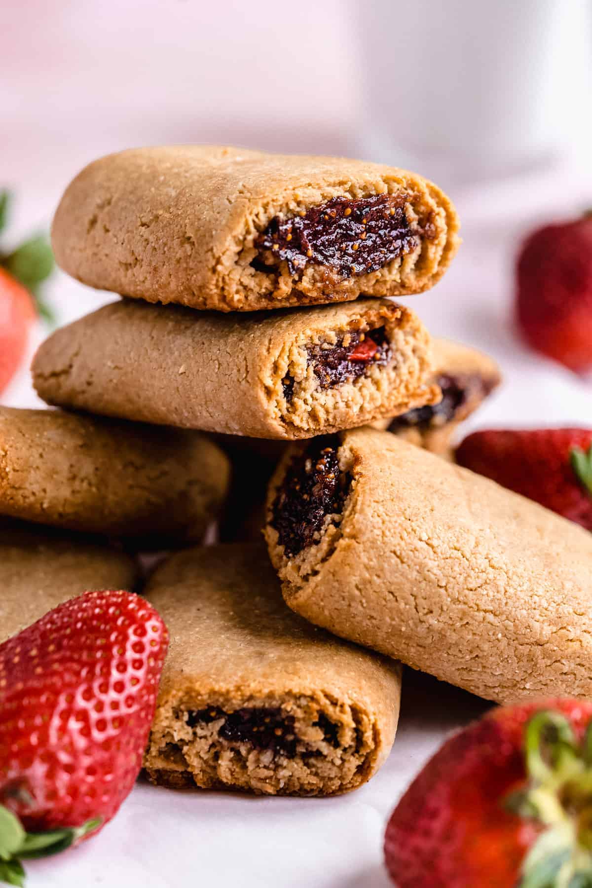 Big stack of fig newtons with red strawberry jam and strawberries on the surface.