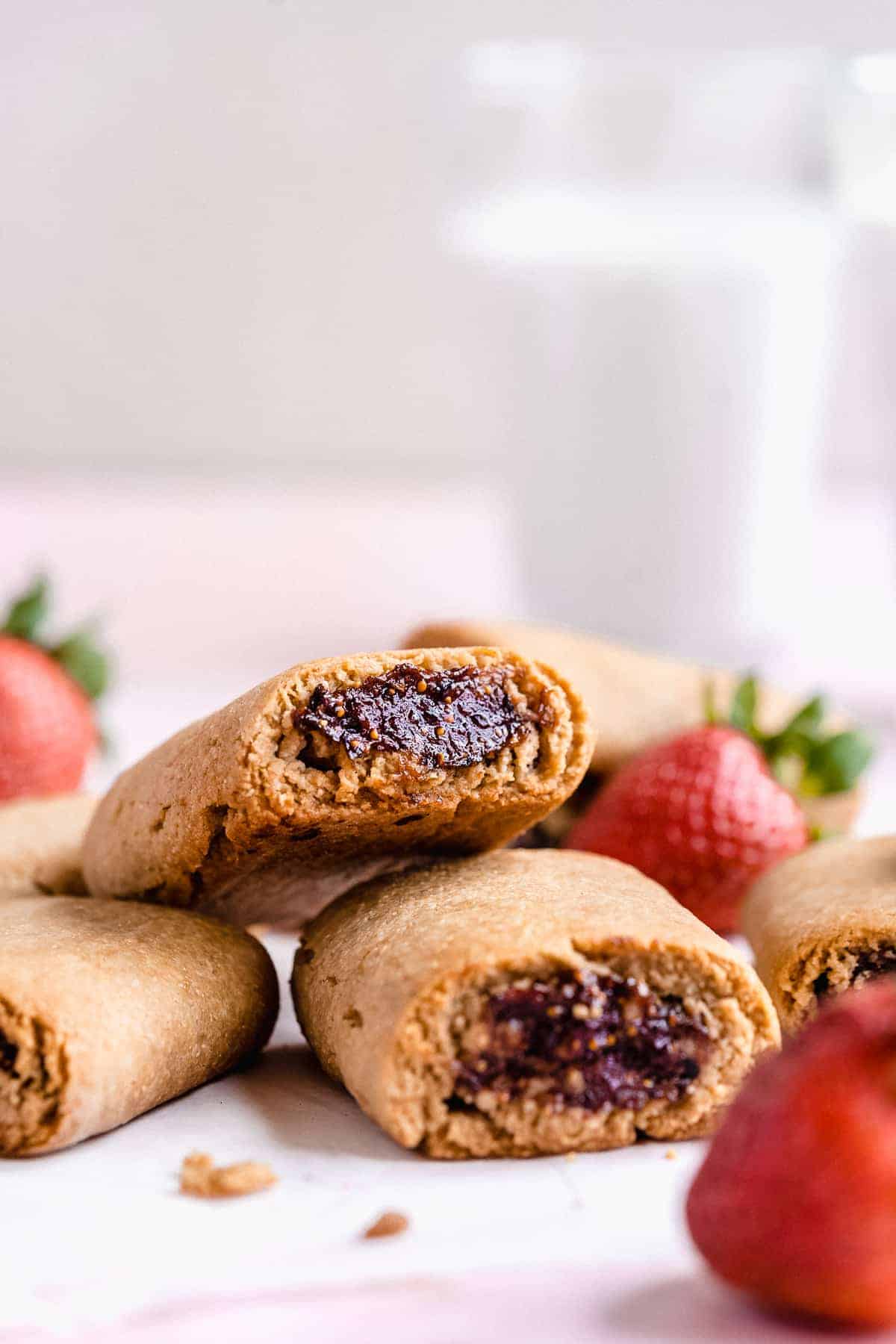 Fig newton cookies scattered on a surface with strawberries in the background.