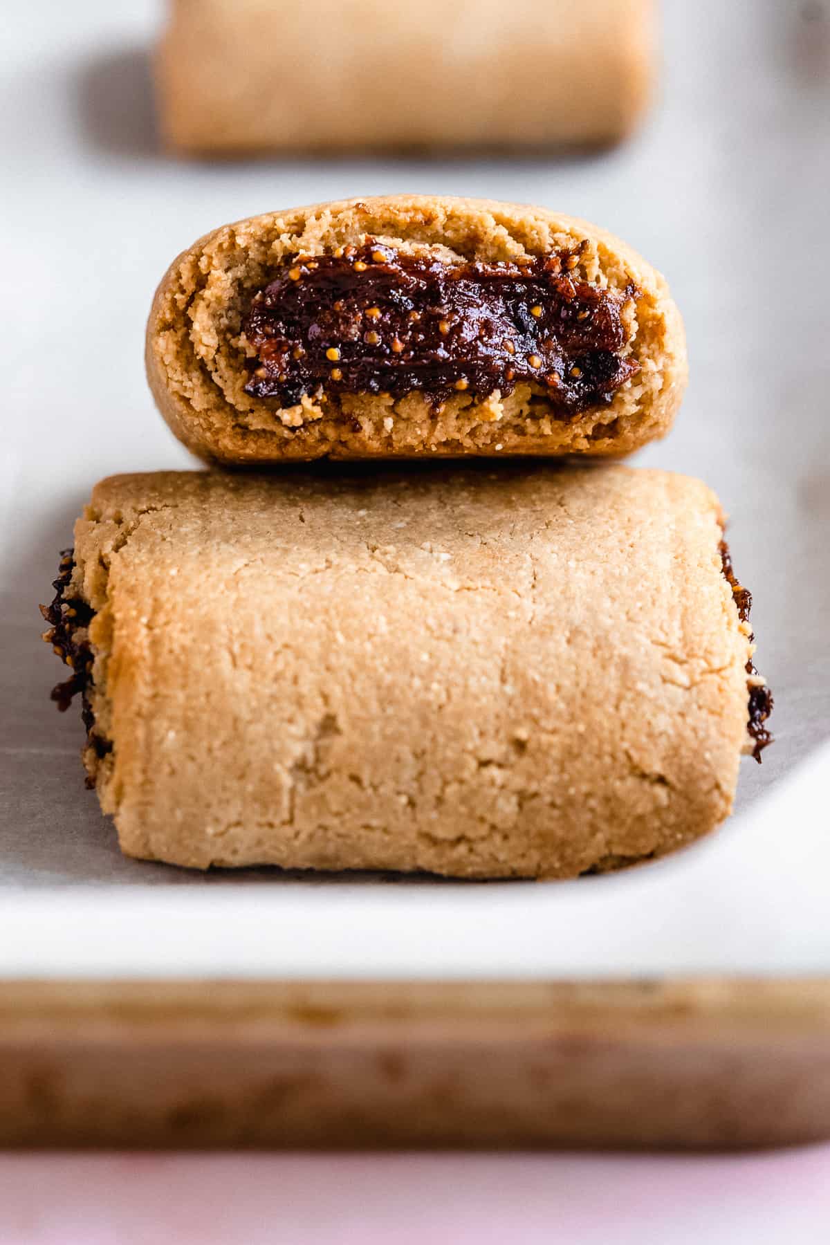 Two fig newton cookies on parchment paper with one on top of the other pointed at the camera.