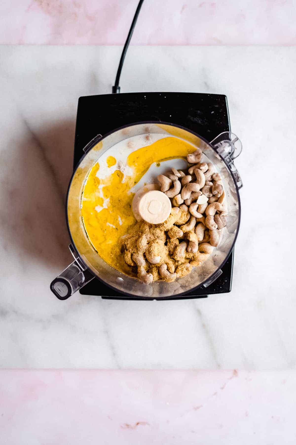 Overhead image of the ingredients in a food processor during the process of making this recipe. Food processor is sitting on a white marble slab.