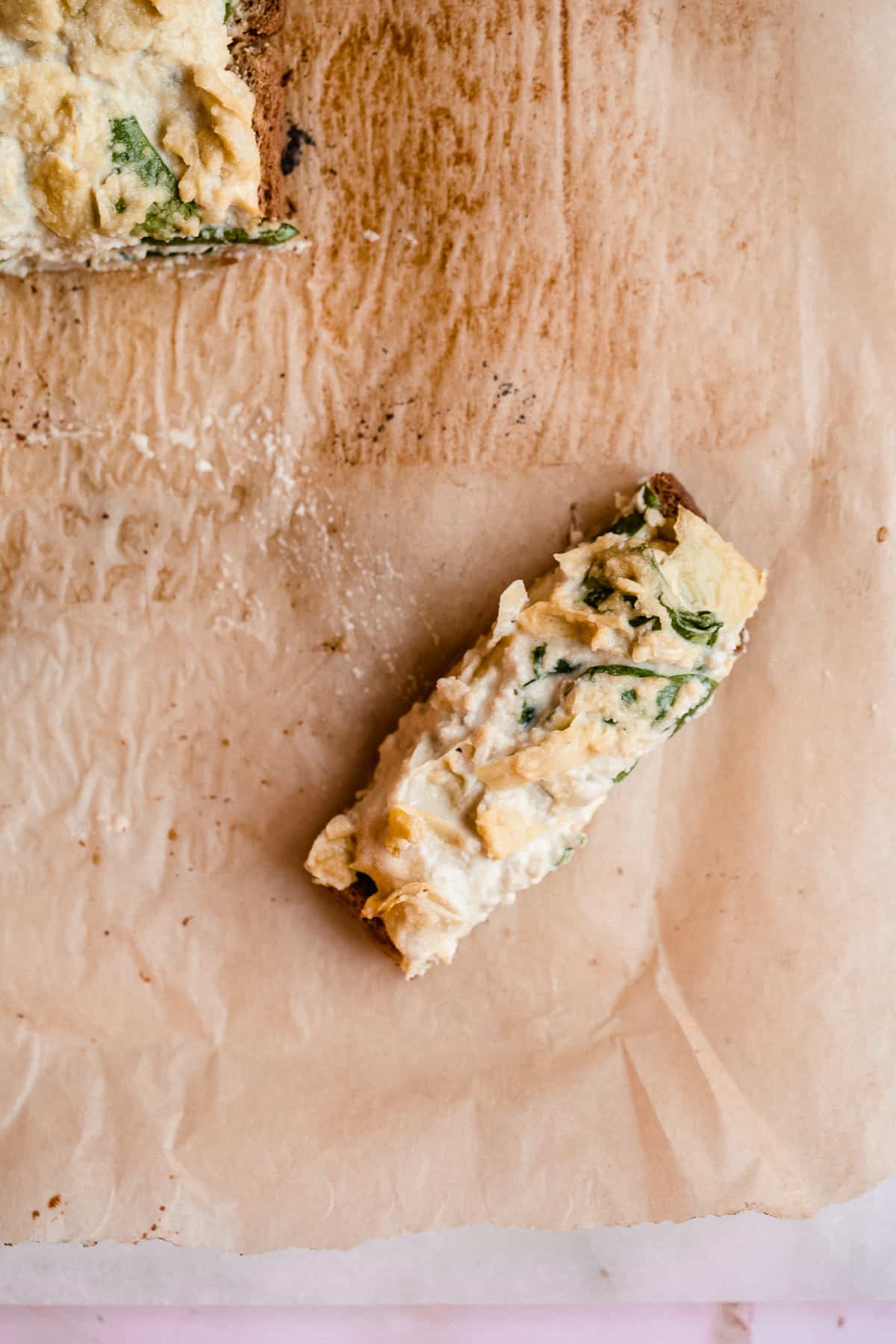 Close up overhead image of a single Spinach Artichoke Toast Stick laying on parchment paper.  