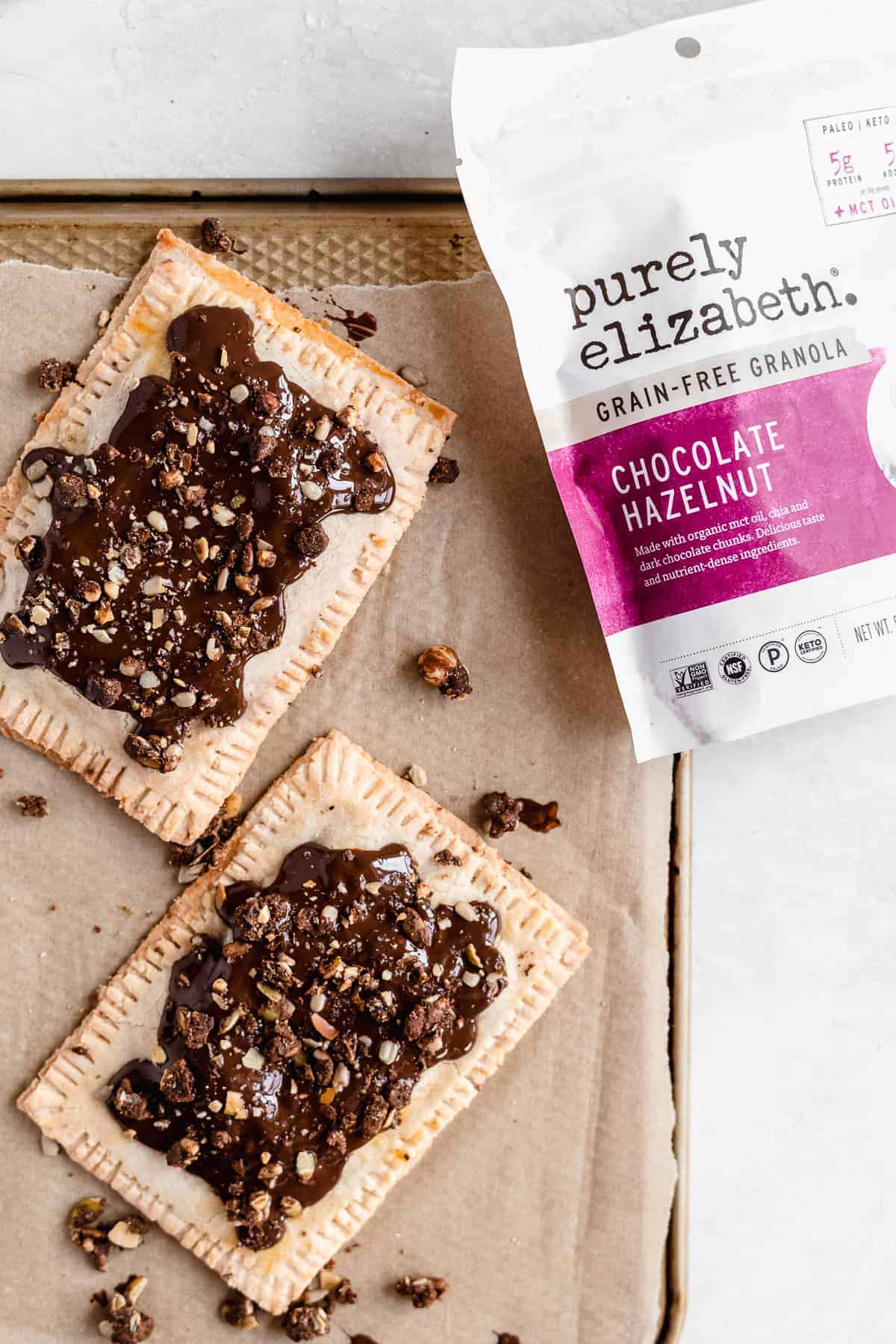 Overhead photo of completed Chocolate Covered Strawberry Pop Tarts arranged on parchment paper.  A bag of Purely Elizabeth Grain Free Granola is laying nearby.  