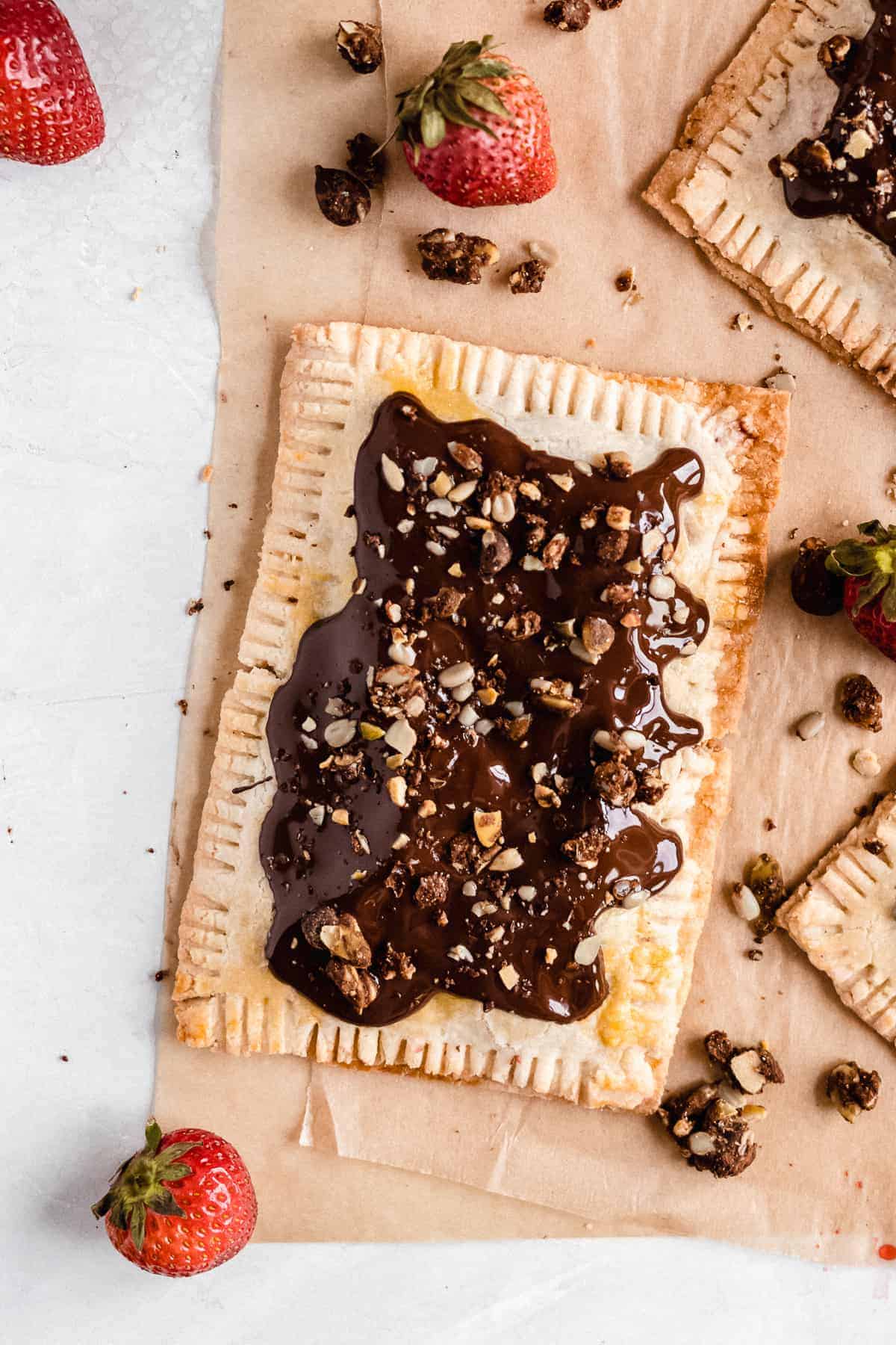 Overhead photo of a single Chocolate Covered Strawberry Pop Tart on parchment paper with several strawberries sprinkled around.  