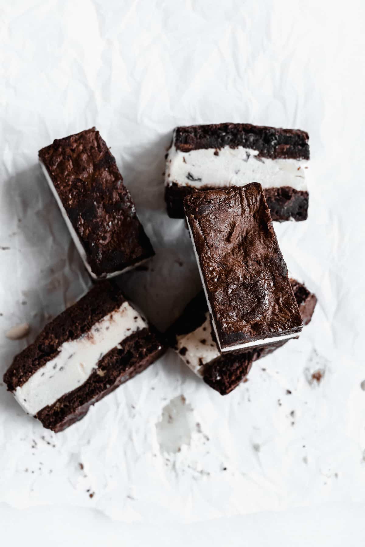 Several Brownie Ice Cream Sandwich squares stacked on top of one another on white parchment paper.