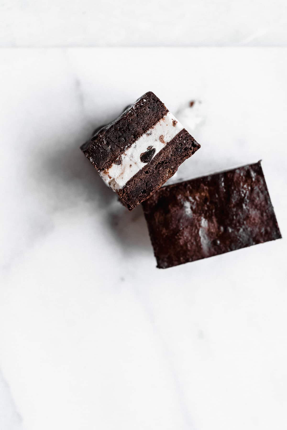 Two Brownie Ice Cream Sandwich squares arranged on a white marble slab.