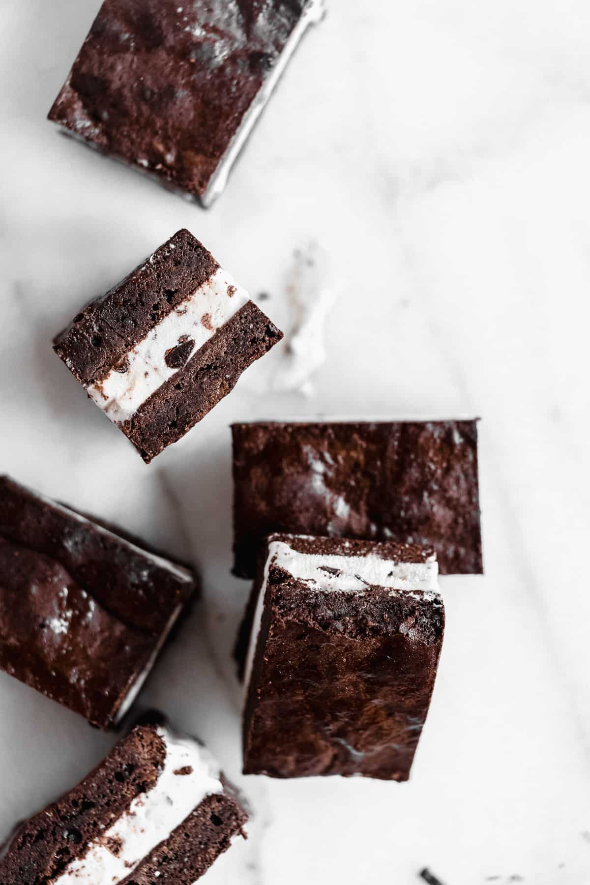 Overhead photo of several Brownie Ice Cream Sandwich squares that are arranged on a white marble slab.  Some squares are resting on their side.  