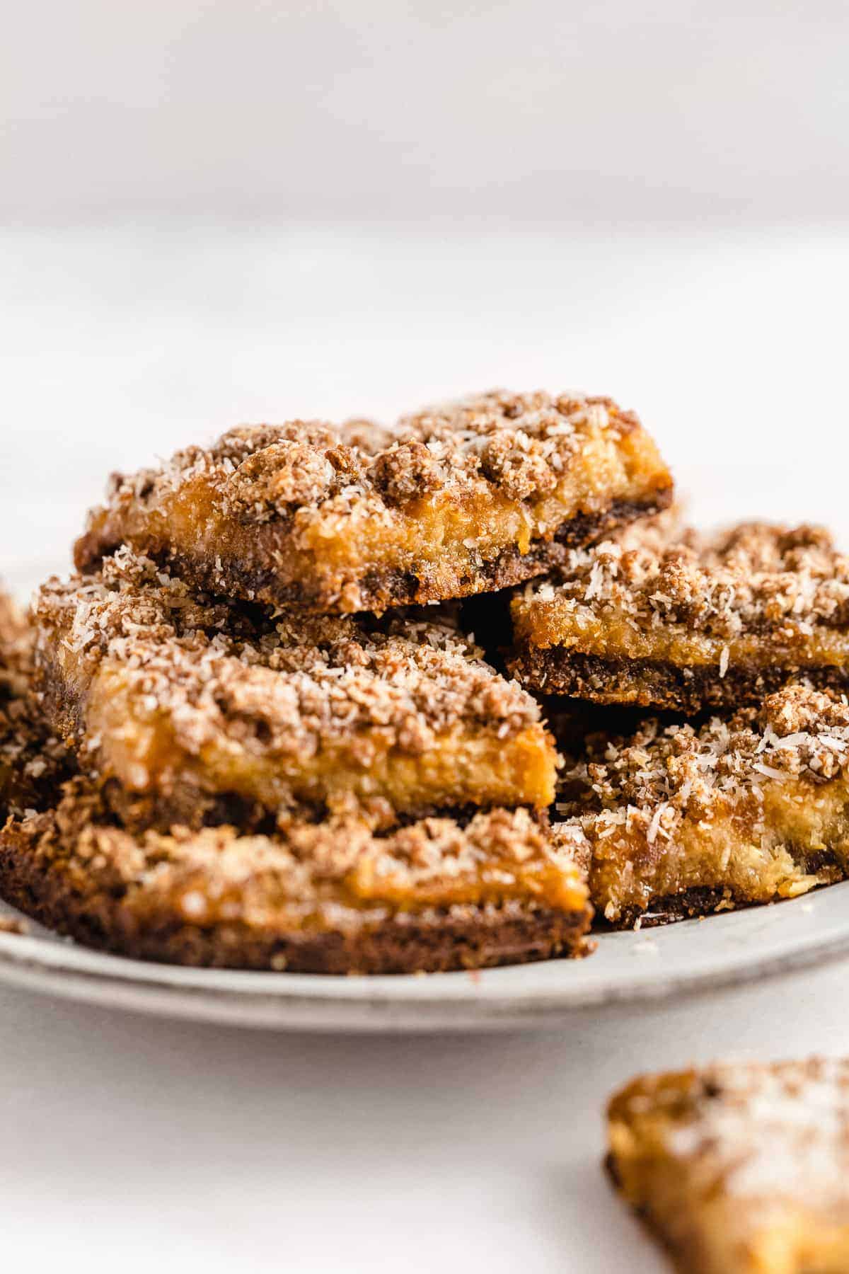 Side view photo of several Pineapple Coconut Crumb Bars stacked on top of one another and arranged on a white plate.