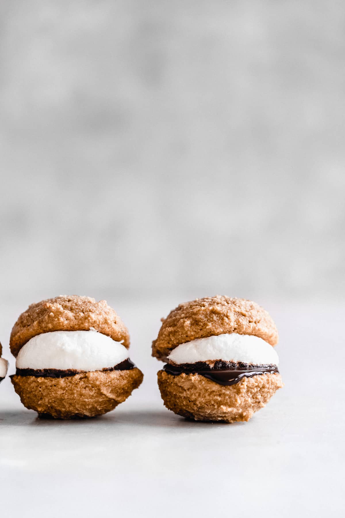 Side view photo of two S'mores Whoopie Pies sitting on a white marble slab to highlight the layers inside.  