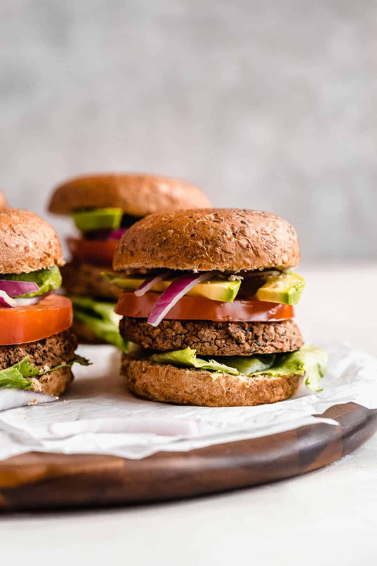 Side view photo of several Black Bean Burgers arranged on parchment paper on a wooden tray.