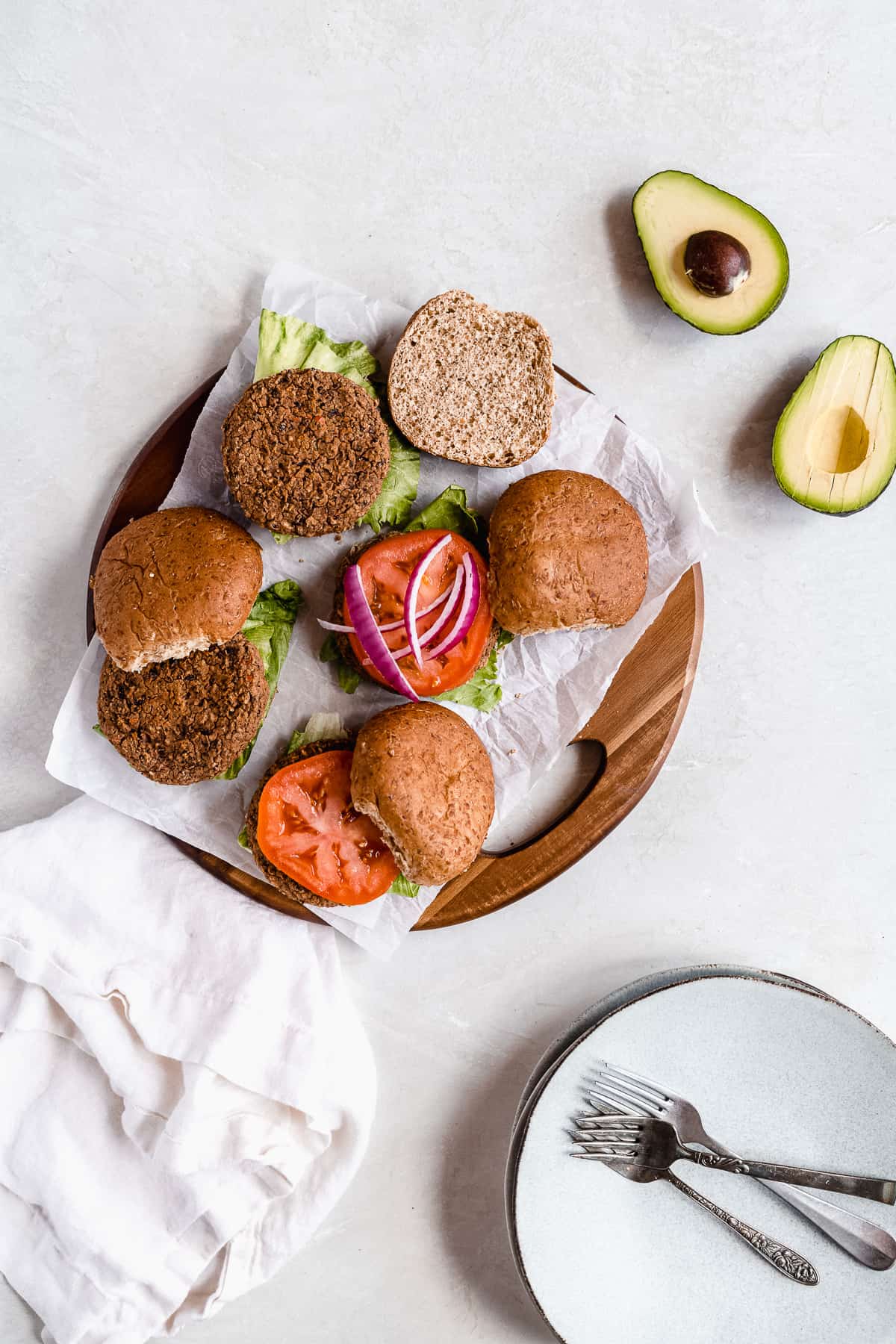Overhead photo of the buns, tomatoes, avocados and onions arranged on parchment paper on a wooden tray in the process of being built into sandwiches.  