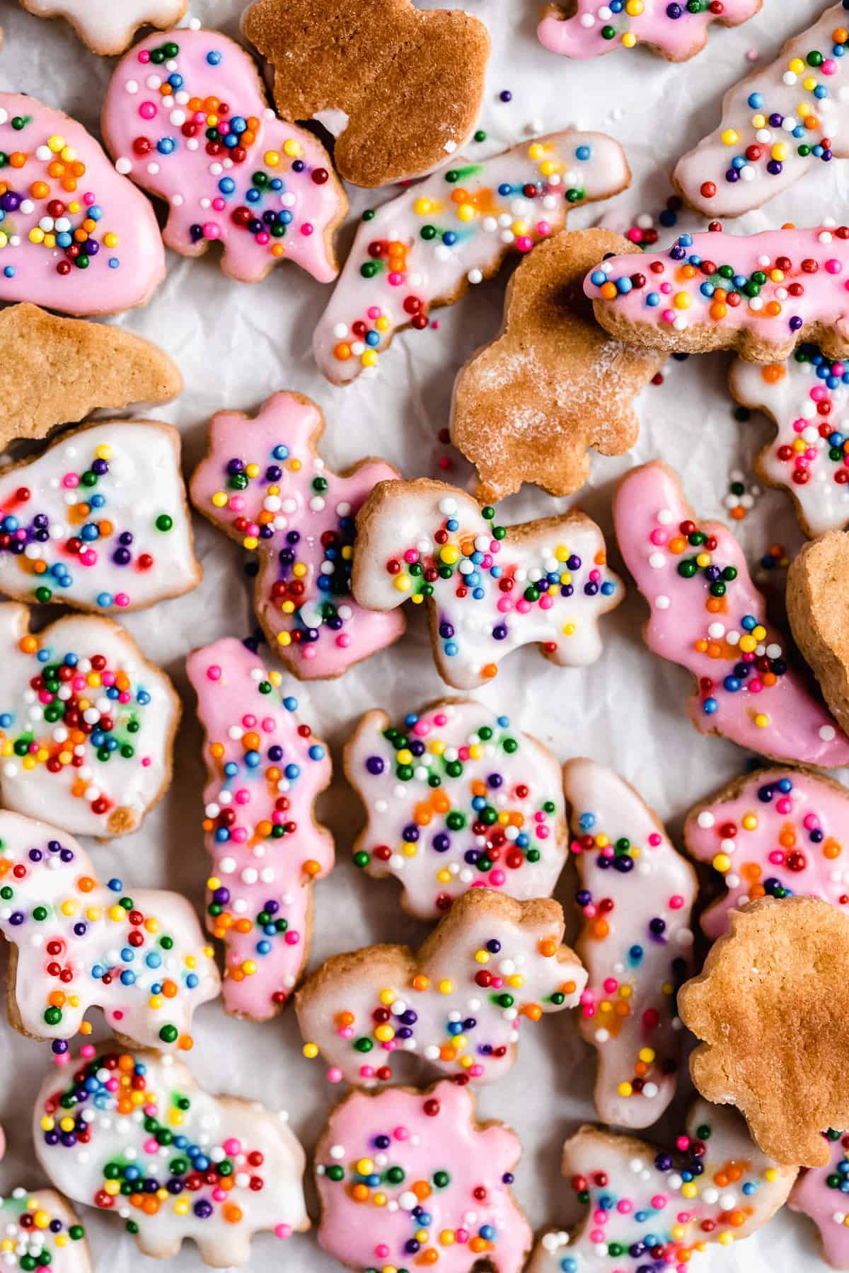 Pink and white animal crackers with sprinkles on a white surface.