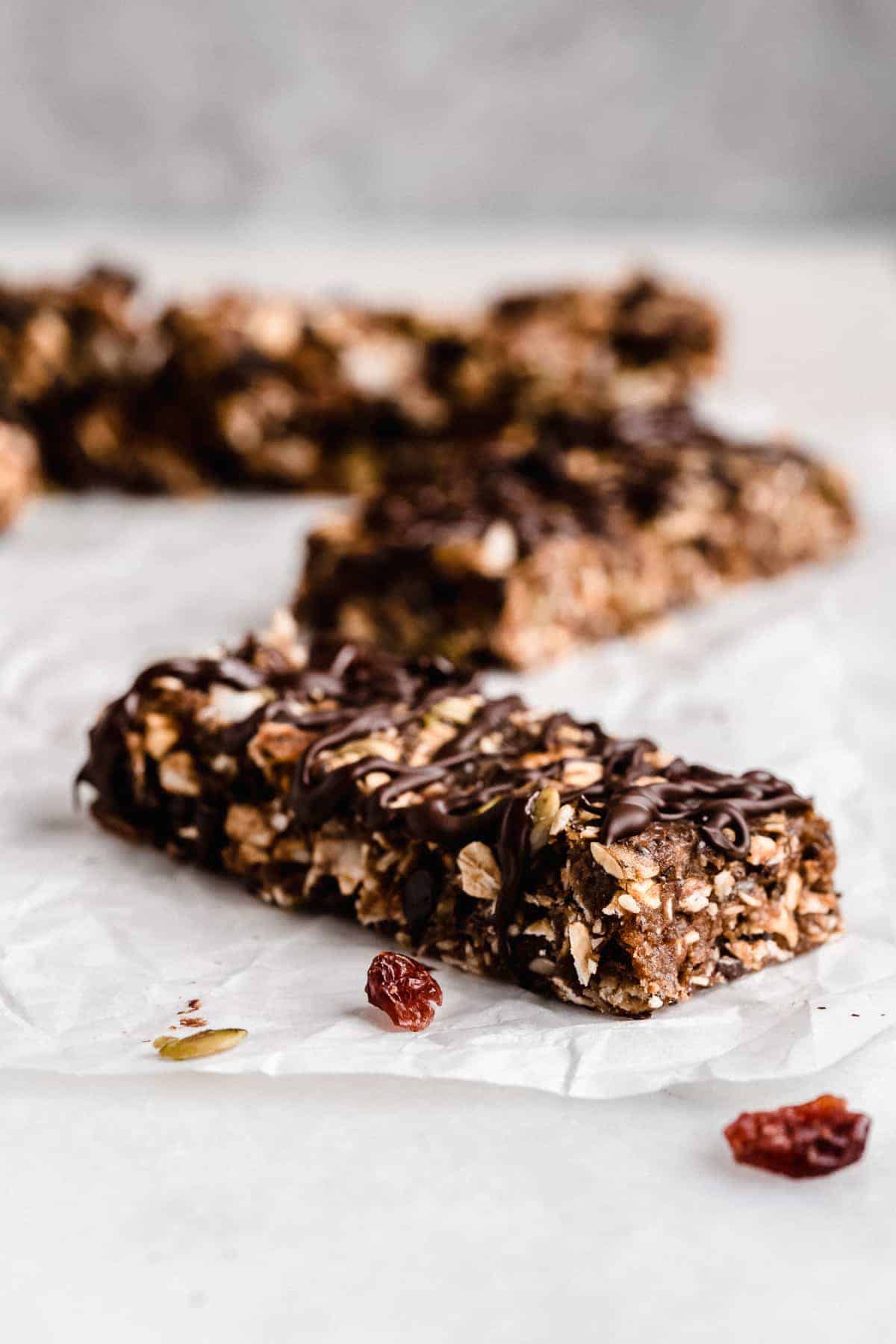 Closeup photo of a single Nut-free Chocolate Granola Bar placed on white parchment paper.  Additional bars can be seen in the background.  