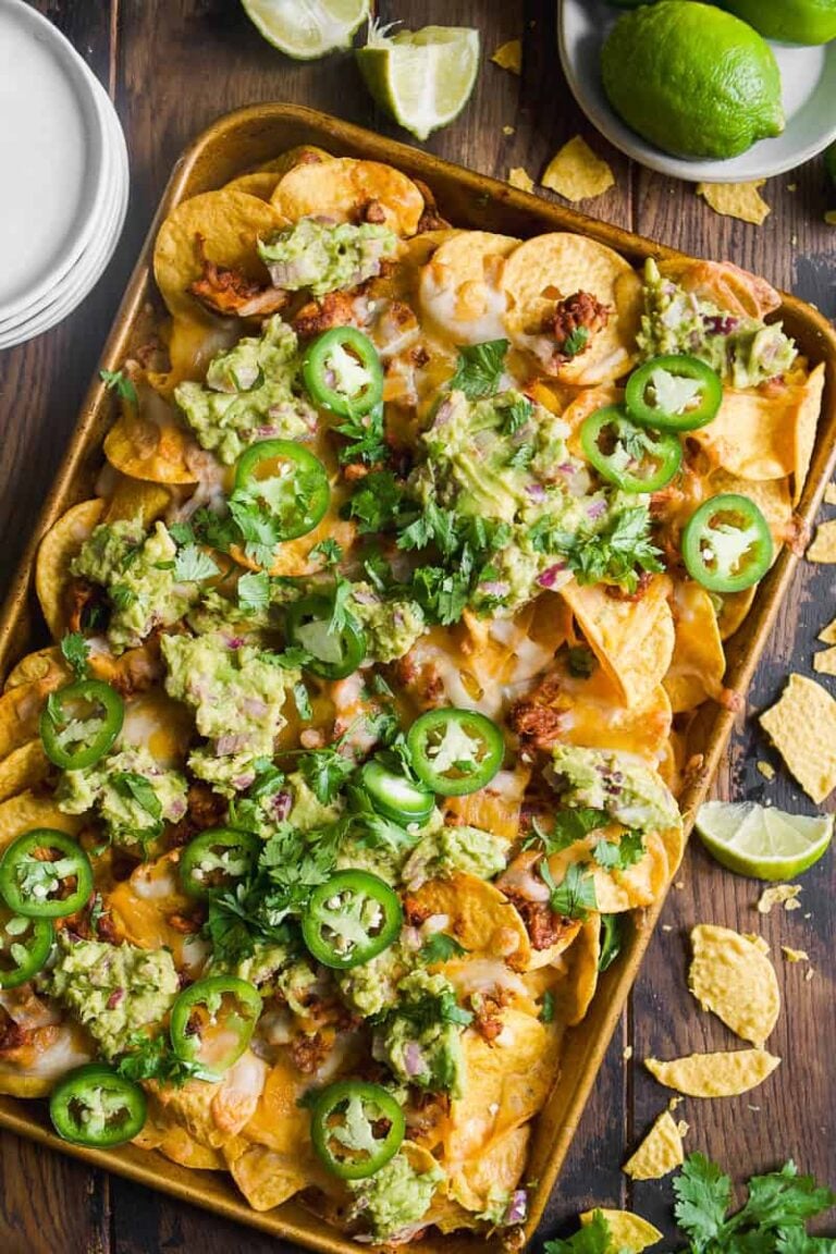 Overhead view of chicken nachos with guacamole, cilantro, and jalapenos on top.