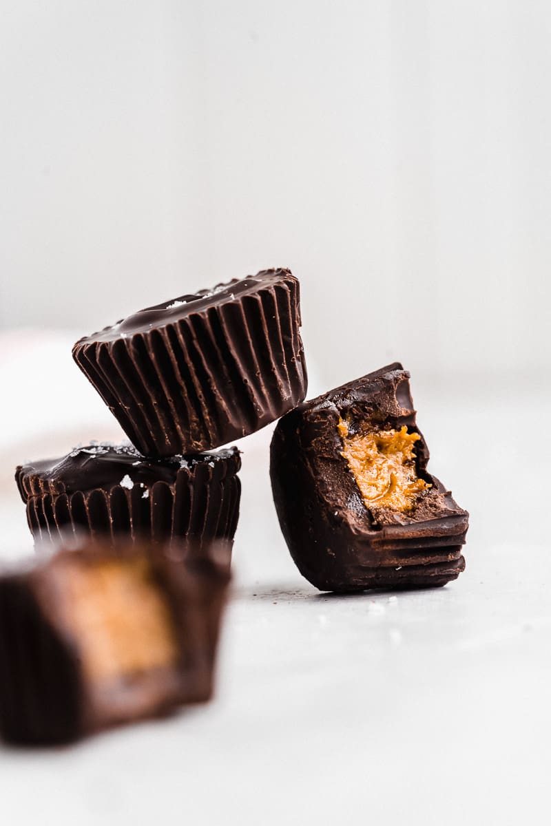 Three chocolate coated pumpkin butter cups. One tipped over with a bite taken out of it.