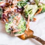 Fork with a bite of broccoli salad with chopped dates, shredded carrots, and avocado mayo.