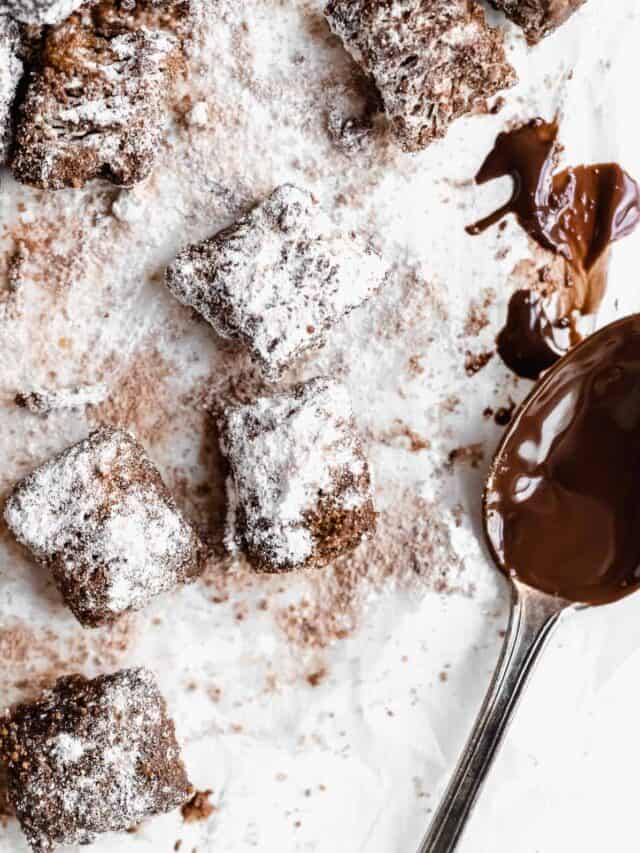 Puppy Chow on parchment paper next to a chocolatey spoon.