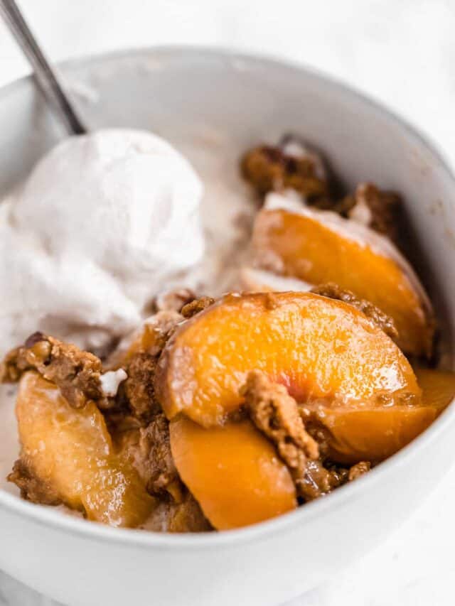 Peach cobbler in white bowl with spoon and ice cream.