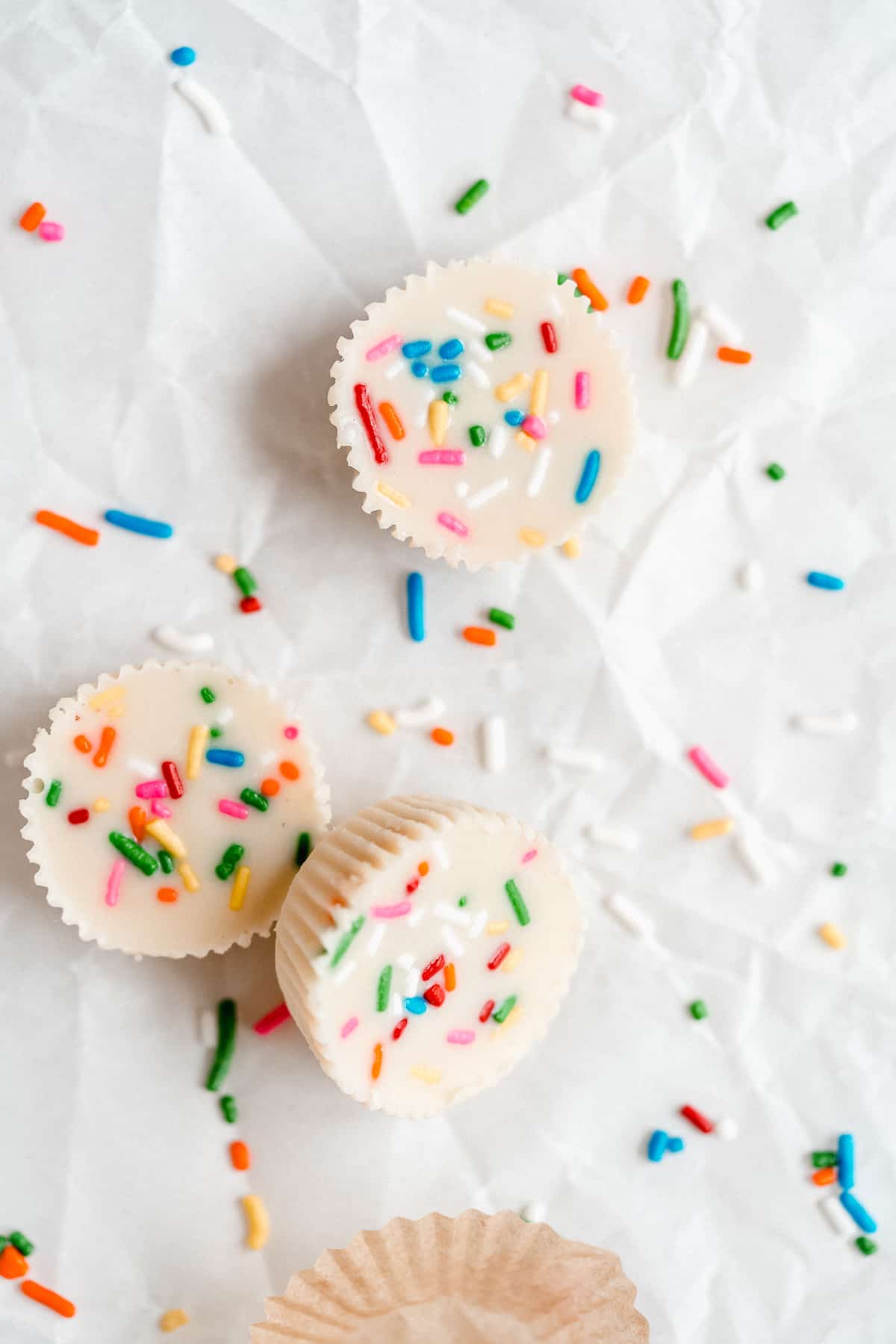 A couple of white chocolate peanut butter cups on white parchment paper with rainbow sprinkles
