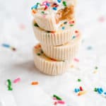 Four white chocolate peanut butter cups stacked on top of one another with a bite taken out of the top and sprinkles on the ground