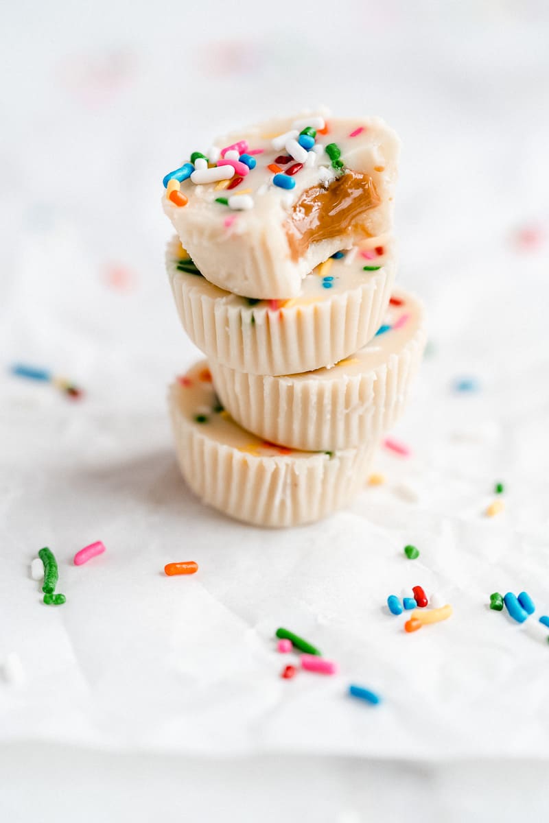 Four white chocolate peanut butter cups stacked on top of one another with a bite taken out of the top and sprinkles on the ground