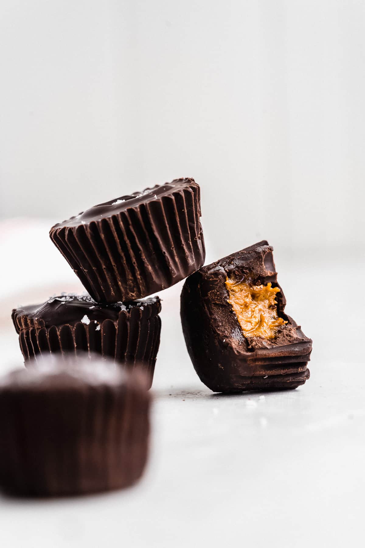 Three chocolate coated pumpkin butter cups. One tipped over with a bite taken out of it.