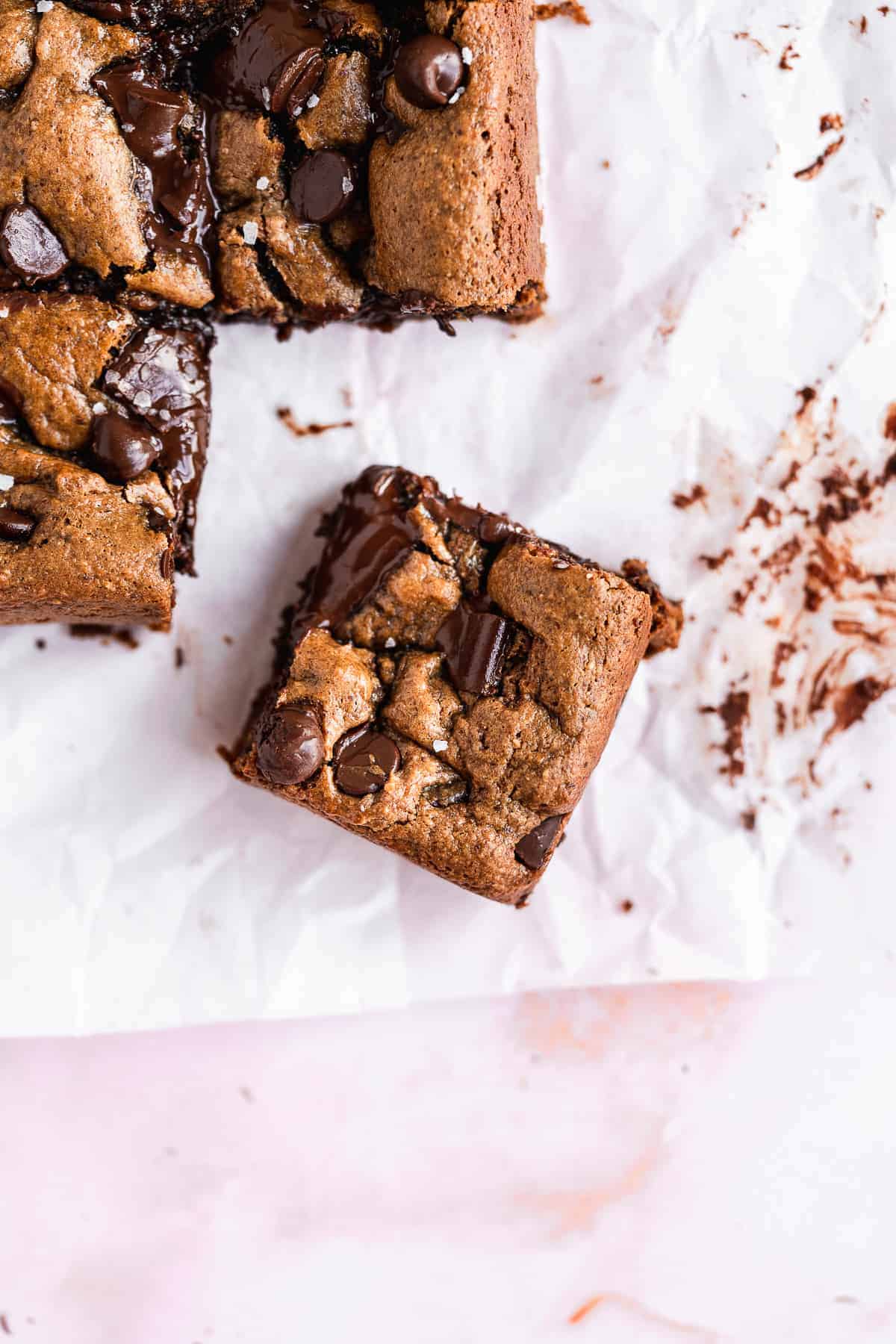 Closeup photo of a single square of the Gluten-free Almond Butter Blondies on white parchment paper.  Several other squares can be seen in the background.  