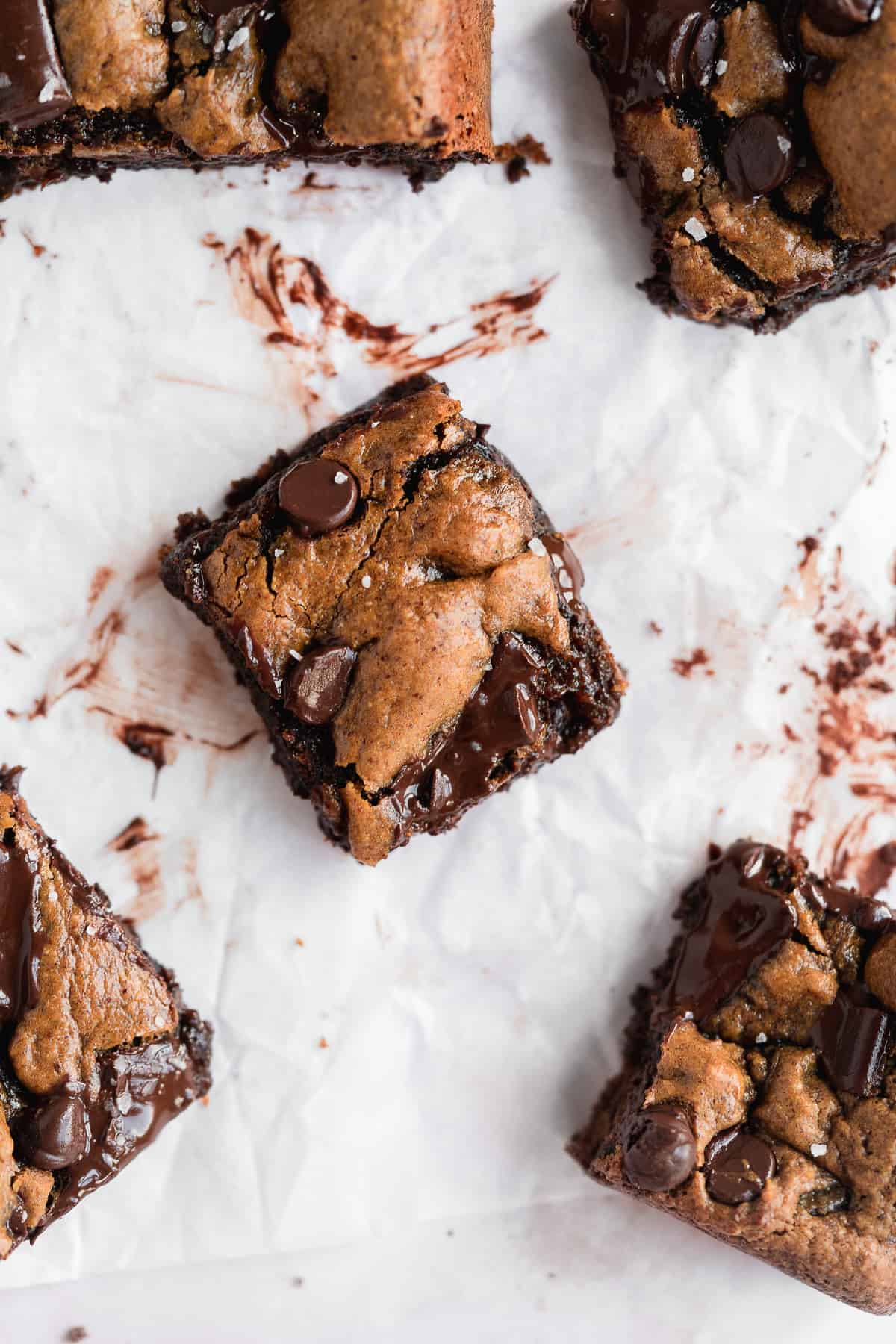 Closeup photo of a single square piece of the Gluten-free Almond Butter Blondies sitting on white parchment paper. Additional square pieces can be seen nearby.