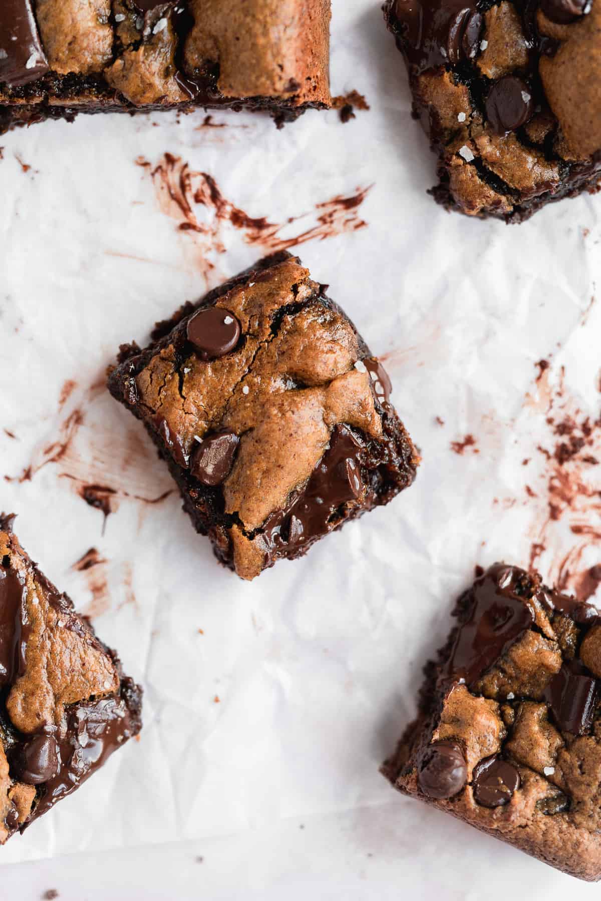 Closeup photo of a single square piece of the Gluten-free Almond Butter Blondies sitting on white parchment paper.  Additional square pieces can be seen nearby.  