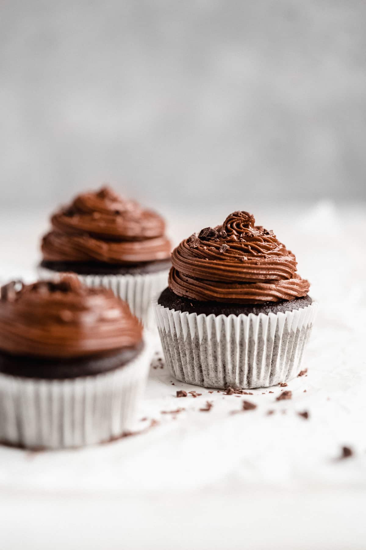 Close up side view photo of three Gluten-free Chocolate Cupcakes sitting on a marble slab.