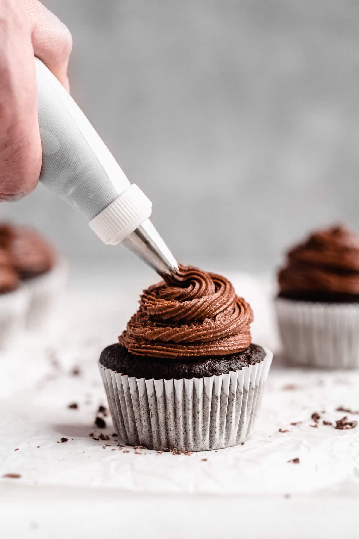 Close up photo of a single cupcake being frosted with an icing tip.
