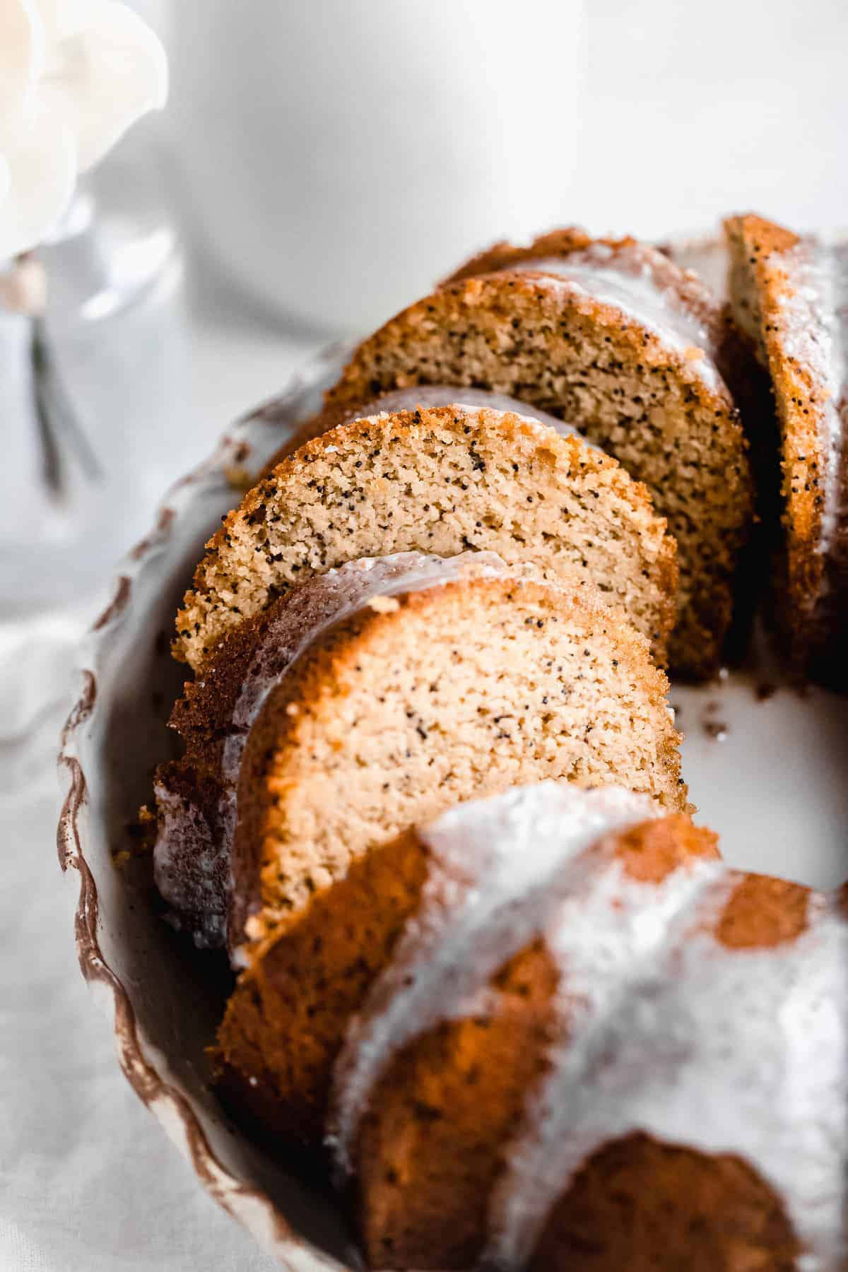 Closeup photo of half of the Citrus-y Gluten Free Lemon Poppy Seed Bundt Cake sliced and sitting on a cake plate.