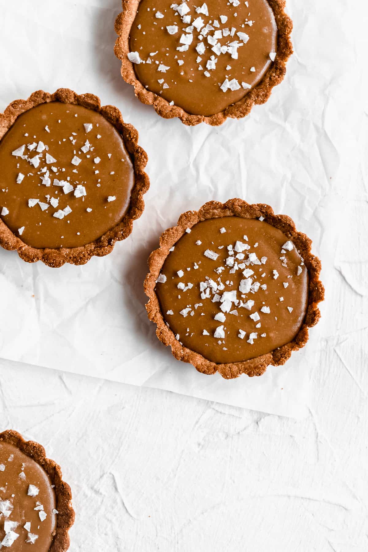 Overhead photo of three Vegan Salted Caramel Tarts arranged on white parchment paper.  