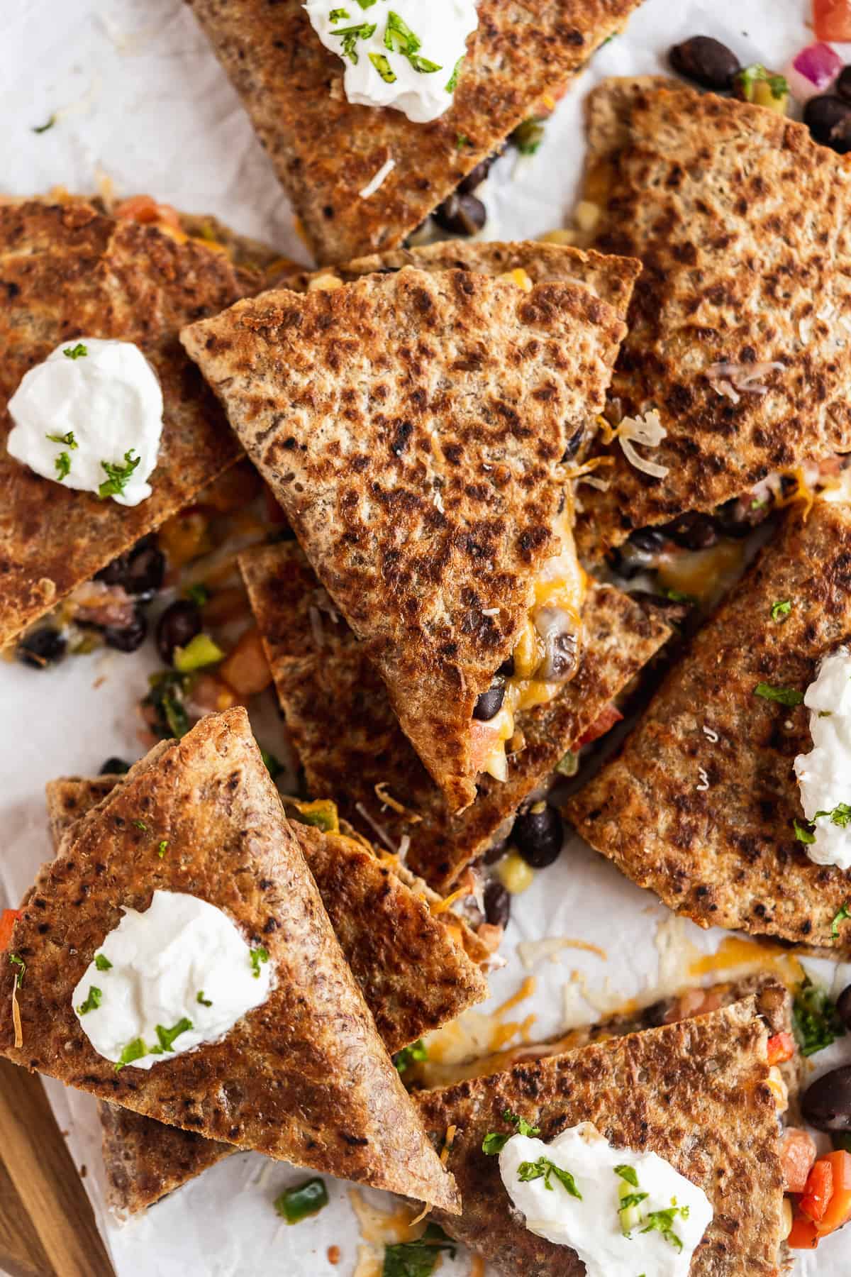 Close up overhead photo of Southwest Quesadilla triangles stacked on parchment paper and ready to be enjoyed.  