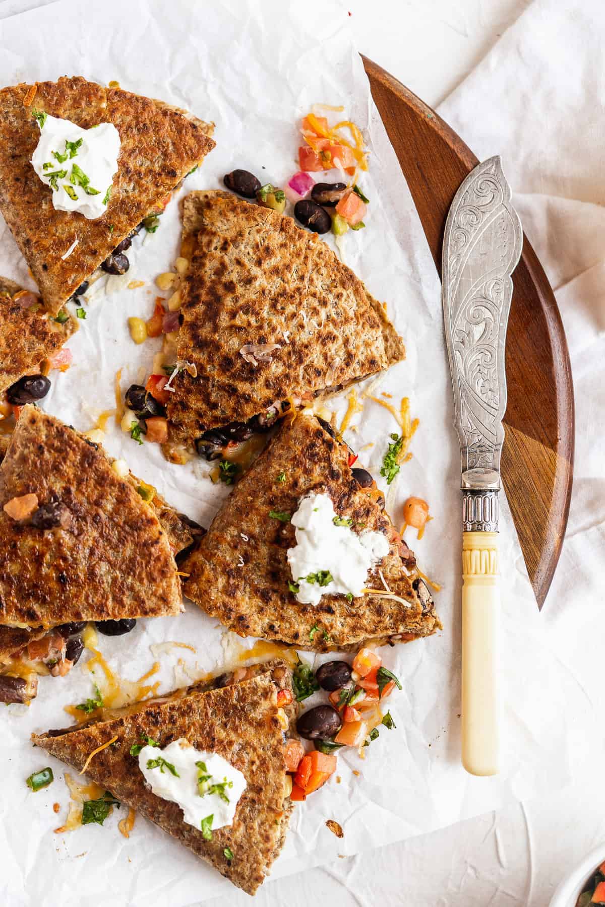 Closeup overhead photo of Southwest Quesadilla triangles on parchment paper on a wooden tray.  A dollop of Greek yogurt is on top of several triangles.  