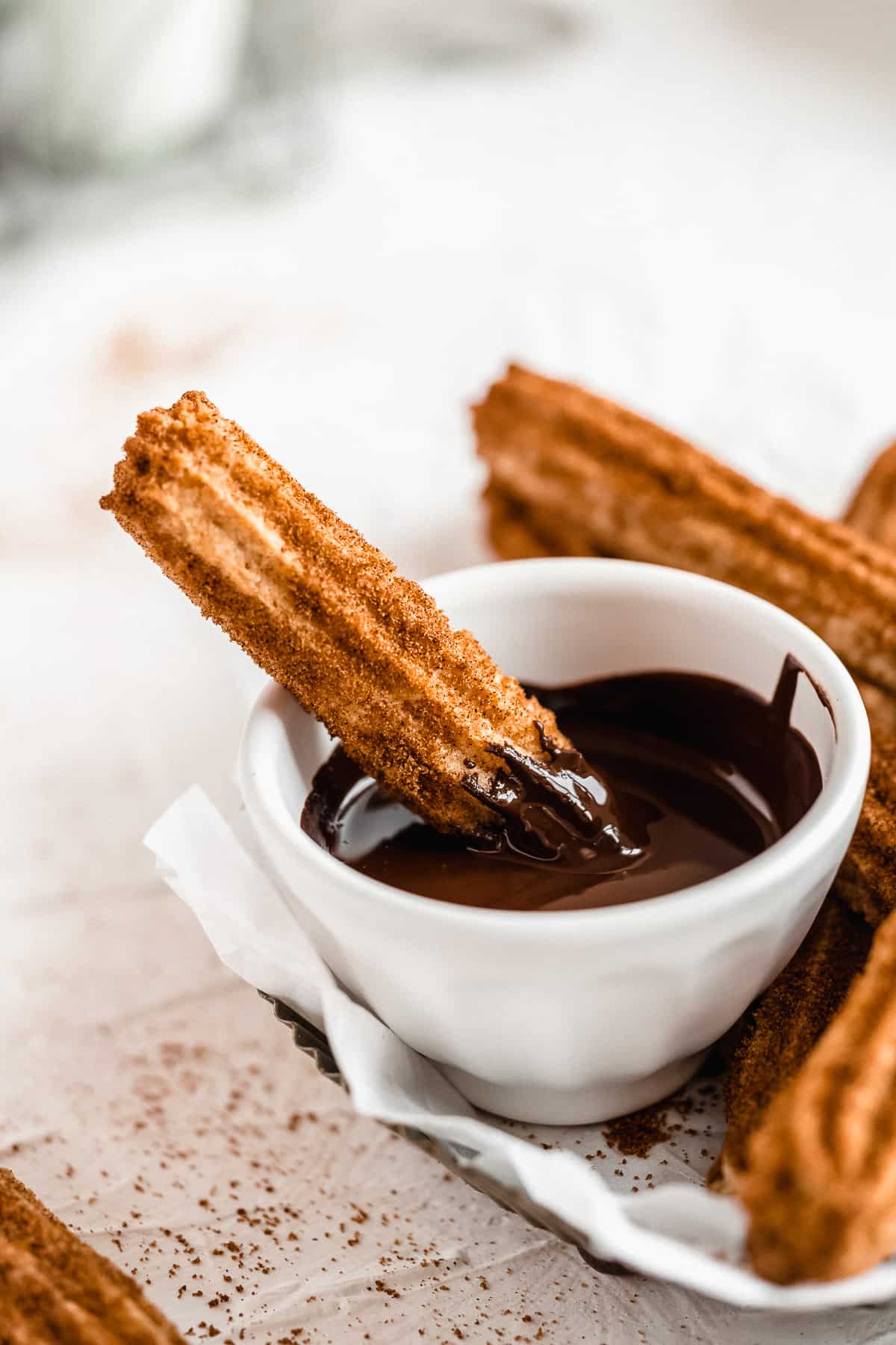 Churro resting in a white bowl of melted chocolate.