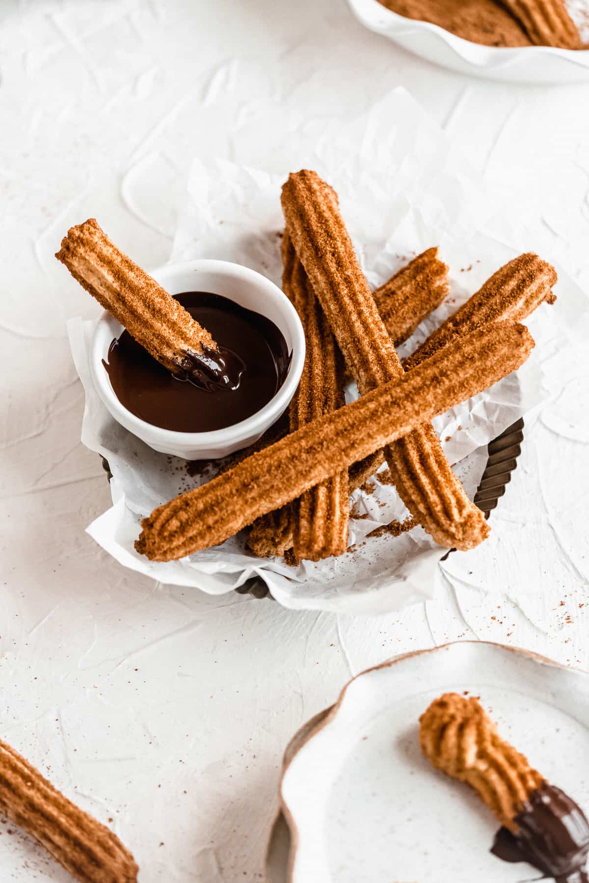 Basket of gluten free churros with one dipped in chocolate.