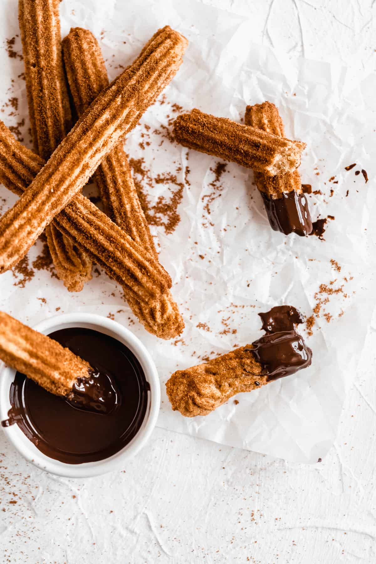 Churros scattered on a white surface with melted chocolate.