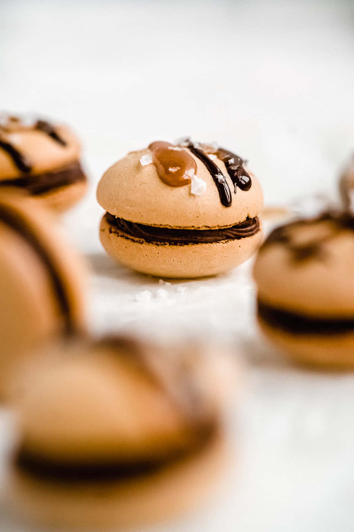 Close up side view photo of several Dark Chocolate Caramel Dairy-free Macarons sitting on white parchment paper.  