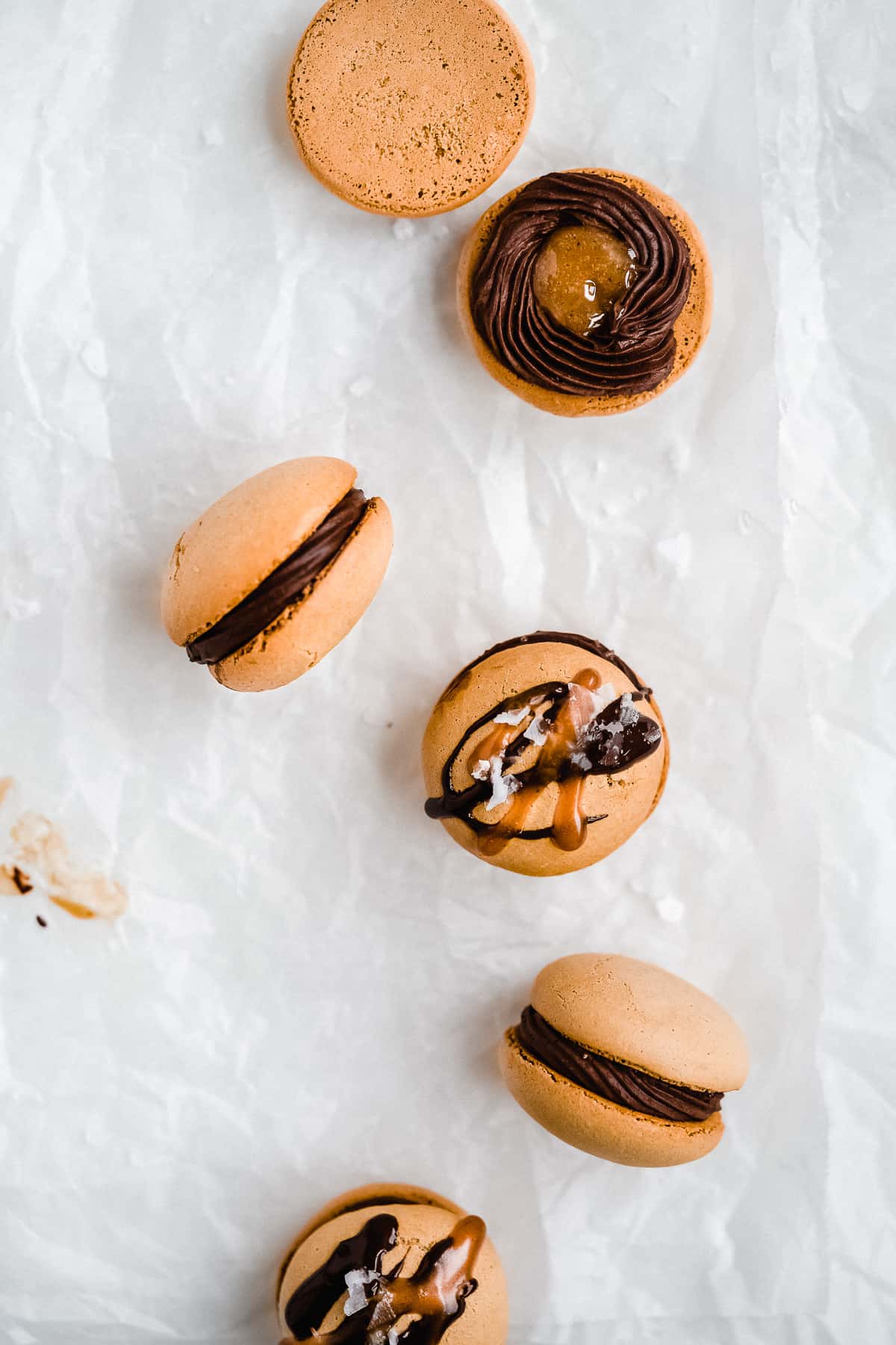 Overhead photo of one of the Dark Chocolate Caramel Dairy-free Macarons taken apart to show the chocolate caramel filling inside.  Another macaron is laying on its side.  